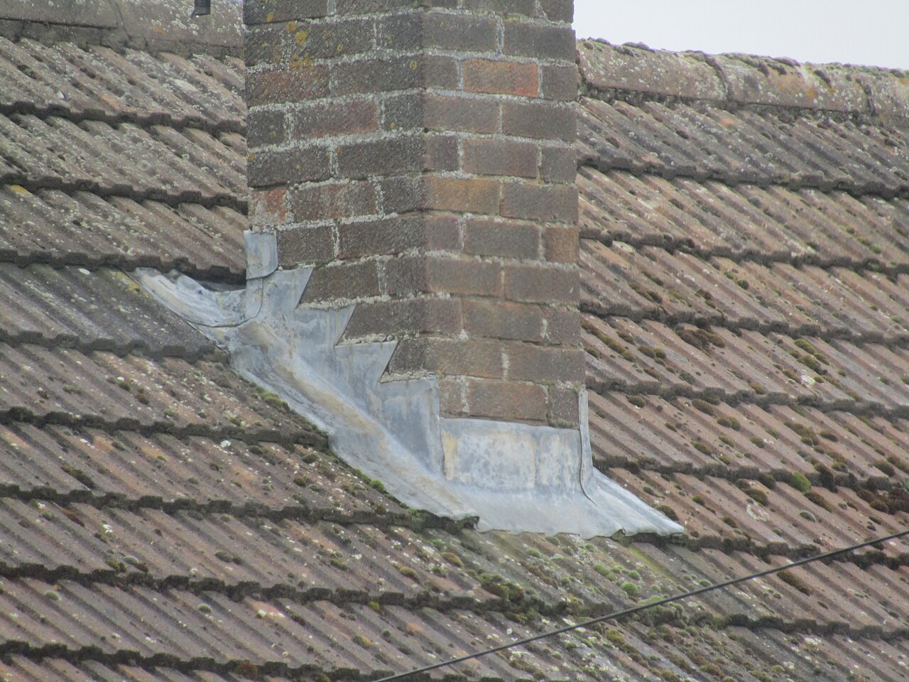 Stepped metal counterflashing sealing the joint where a brick chimney meets the roof, the detail that keeps Ogden freeze-thaw water out